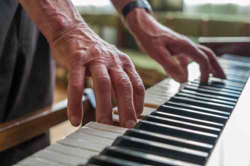 An old man with a worker's hands playing the piano. close up